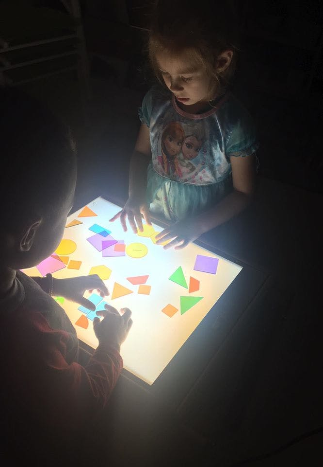 Two children playing with colorful shapes on a light table