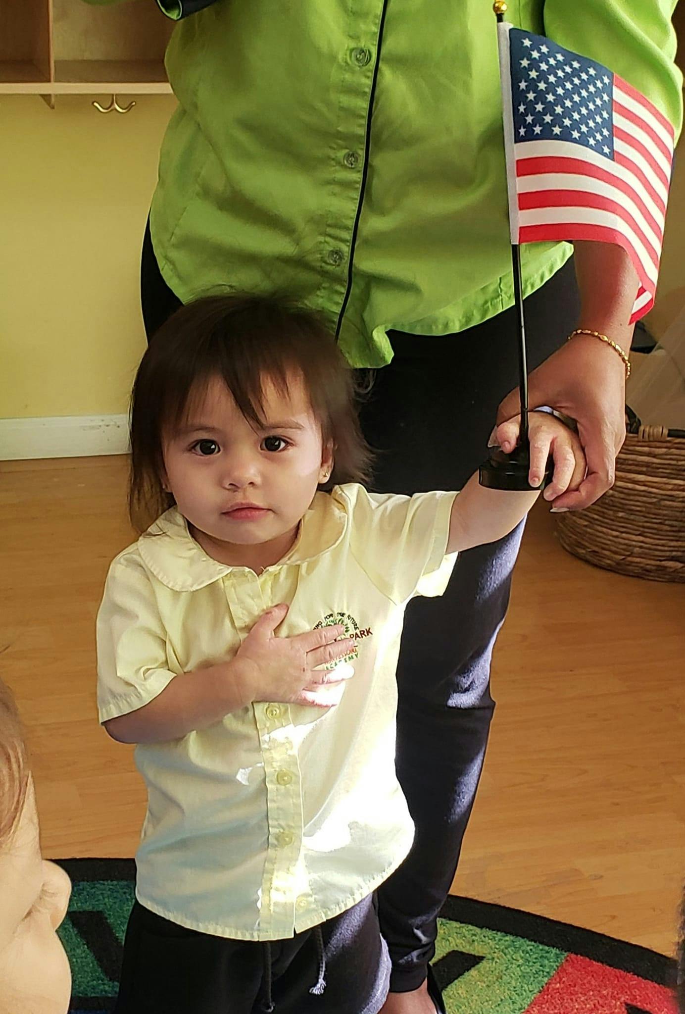 Child holding a small American flag with a person standing behind