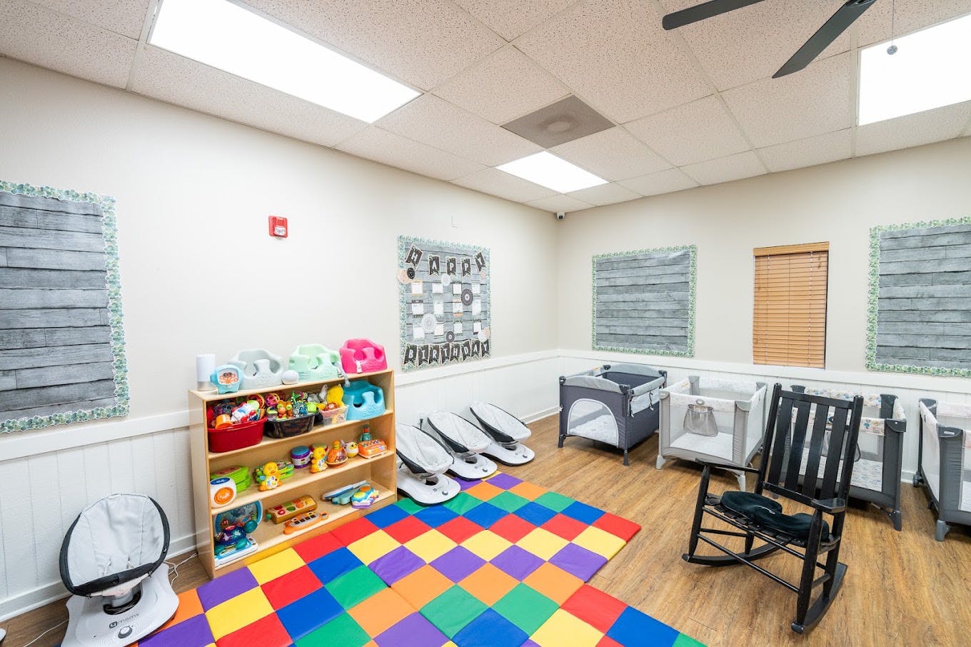 Childcare room with baby gear, play mats, and cribs