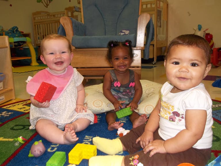 Three babies sitting on a rug with toys
