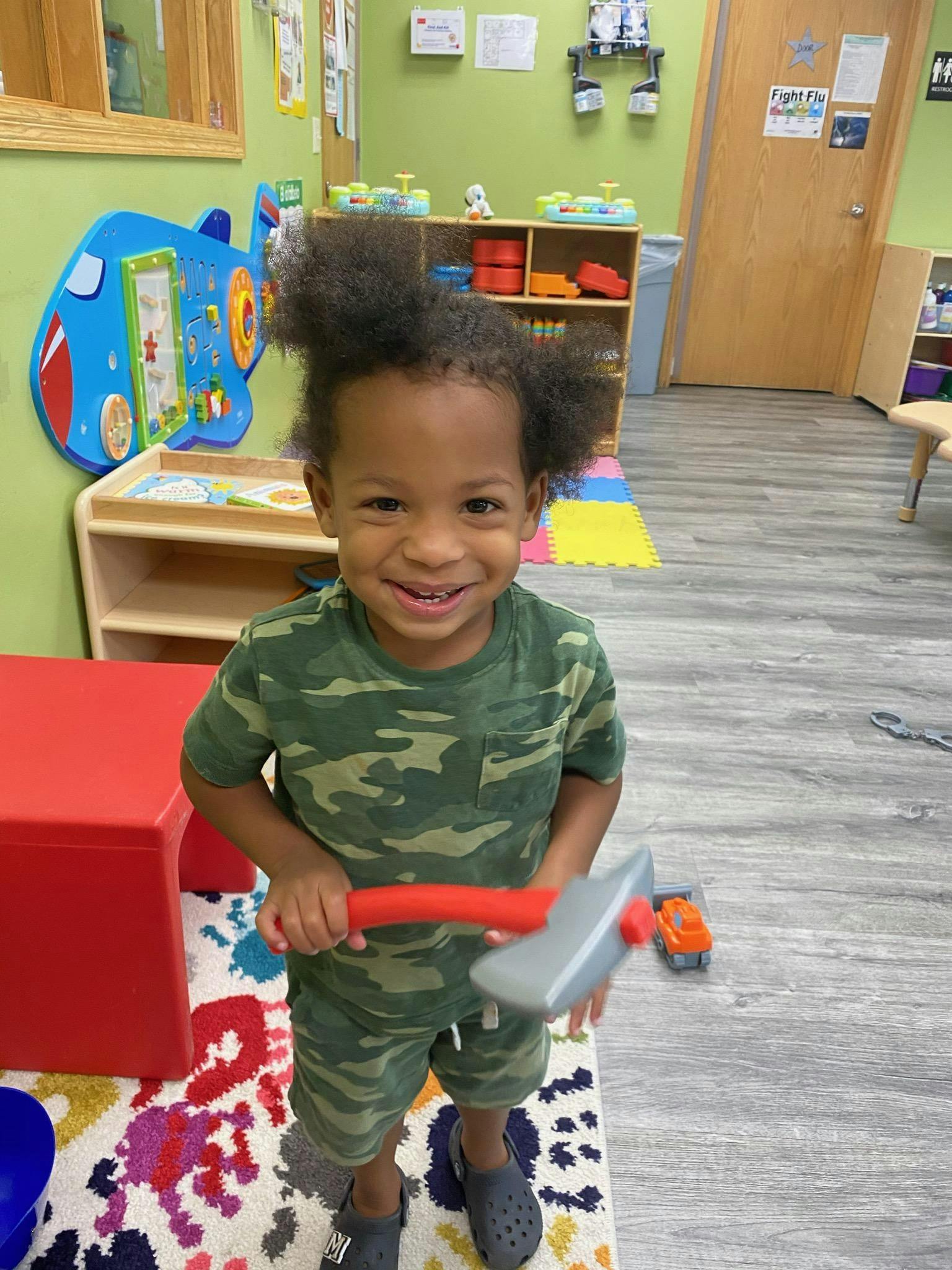 Child in camouflage outfit holding a toy axe