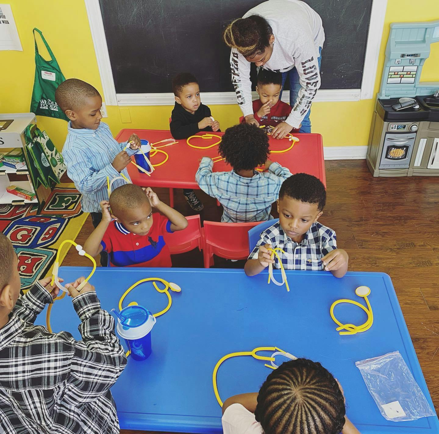 Adult supervising children playing with toy stethoscopes at tables