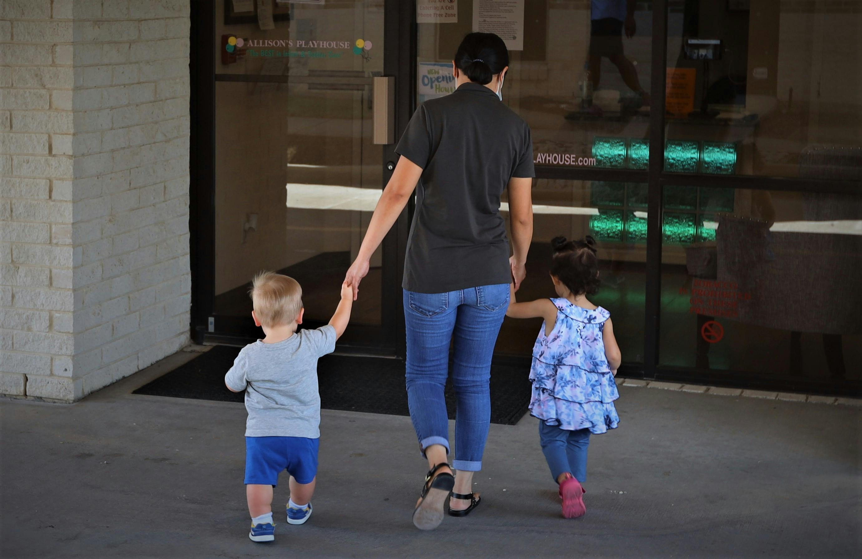 Person holding hands with two children walking away from the camera