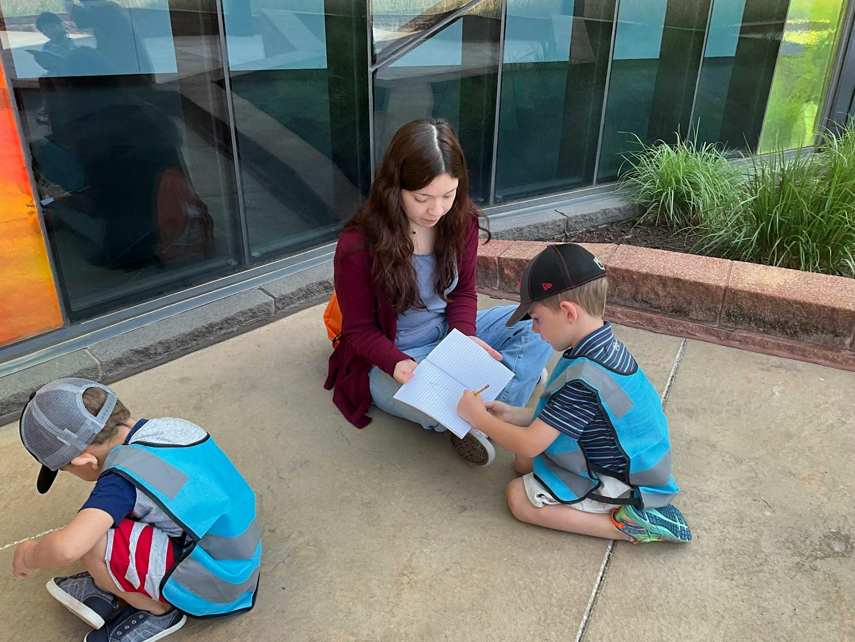 Person and two children sitting on the ground looking at papers
