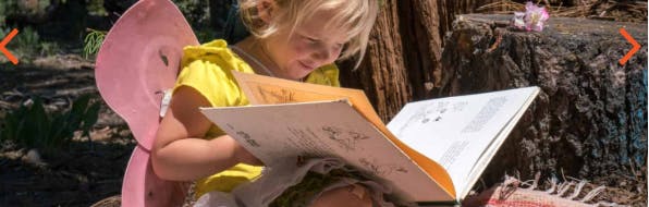 Child wearing pink wings reading a book outdoors