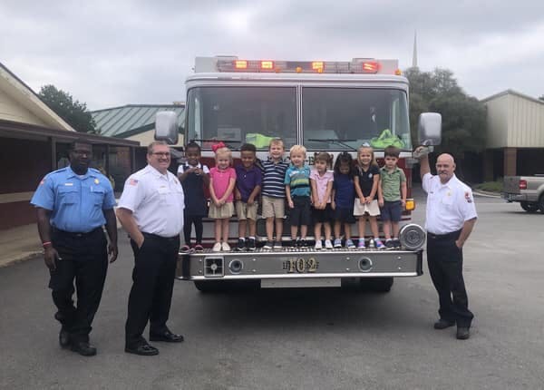 Three adults and multiple children standing on and in front of a fire truck
