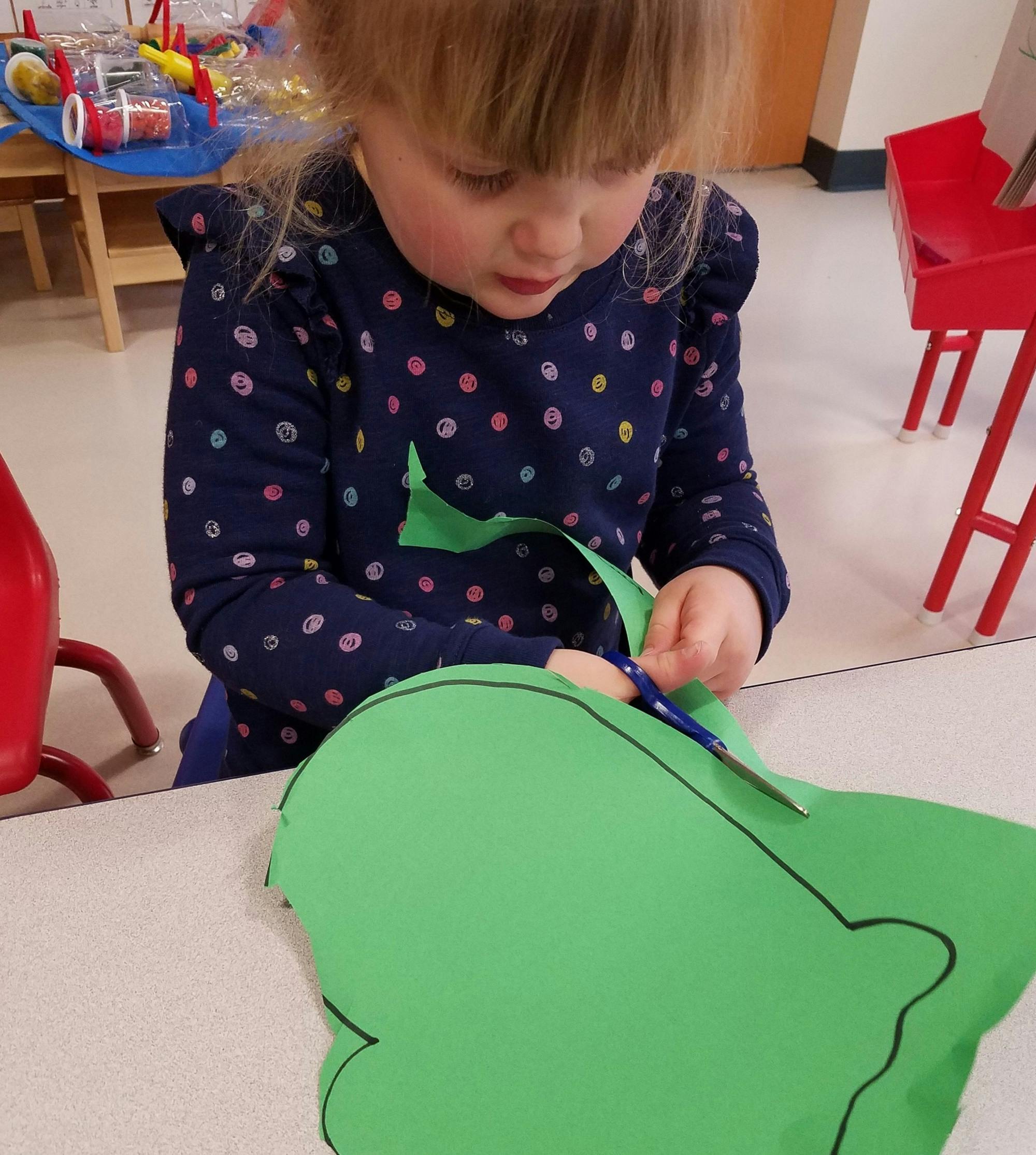 Child cutting green paper with scissors