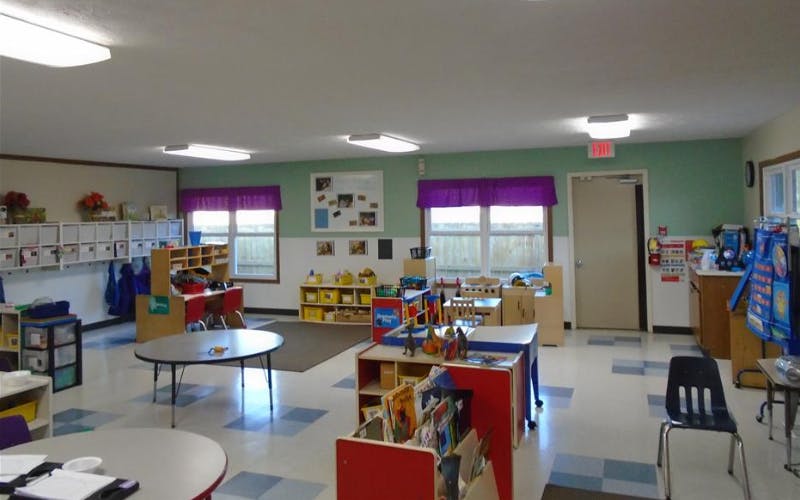 An empty daycare room with tables, chairs, and cubbies