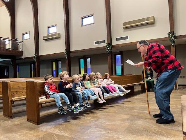 Adult speaking to a group of children sitting on a pew
