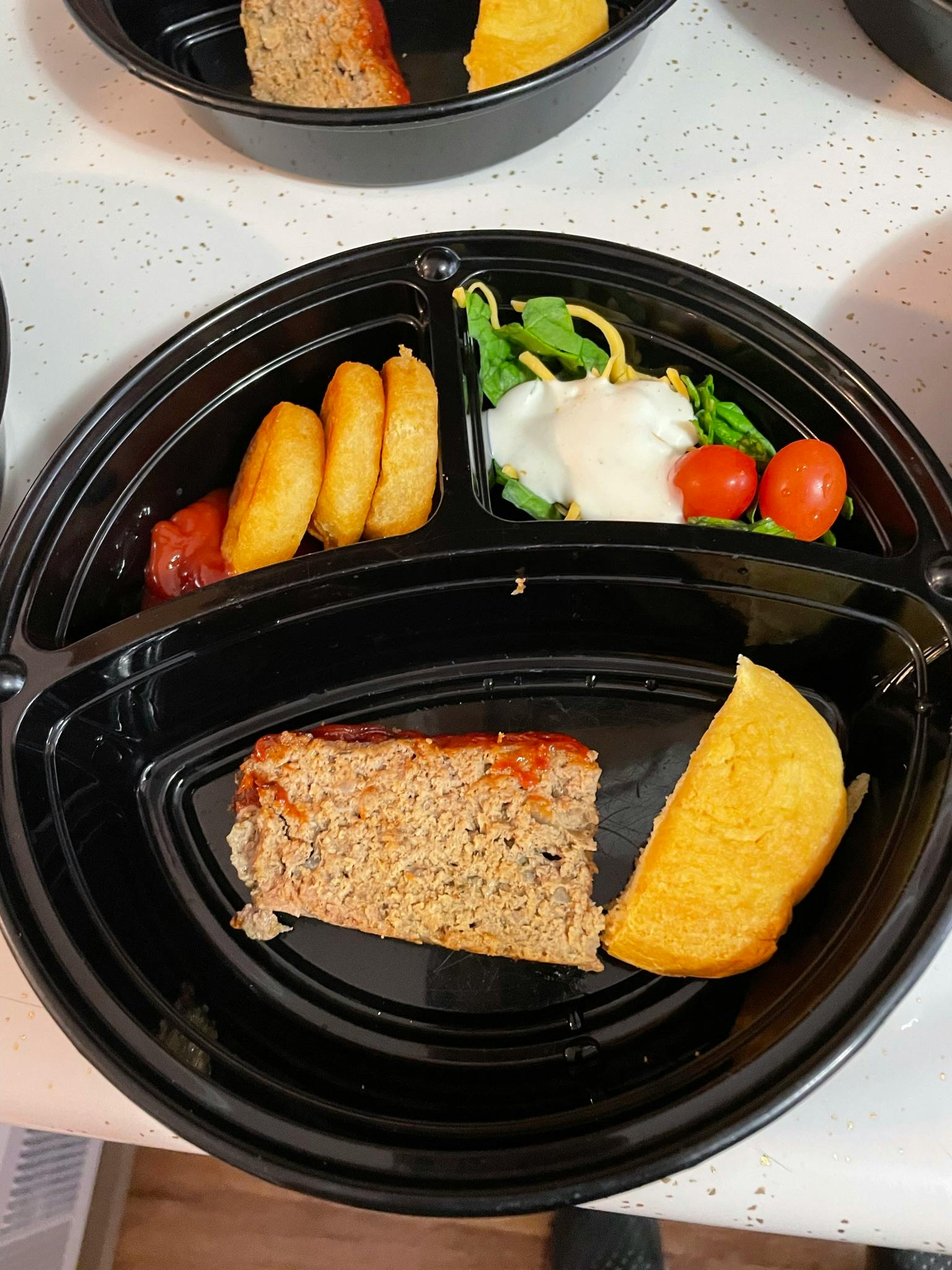 Meatloaf, cornbread, potato wedges, and salad in a divided container