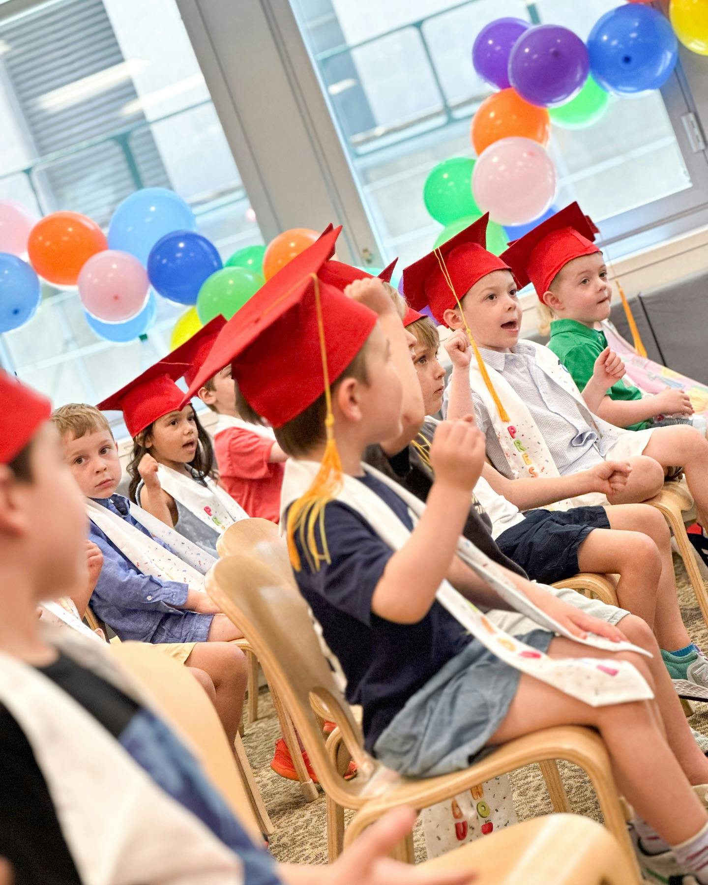 Children in graduation caps and gowns sitting in chairs