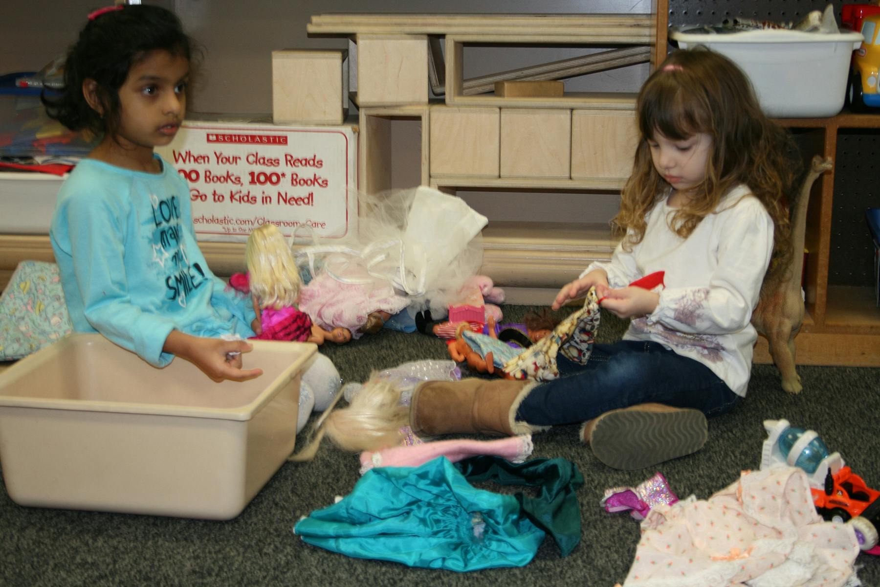 Two children sitting on the floor surrounded by clothes and toys