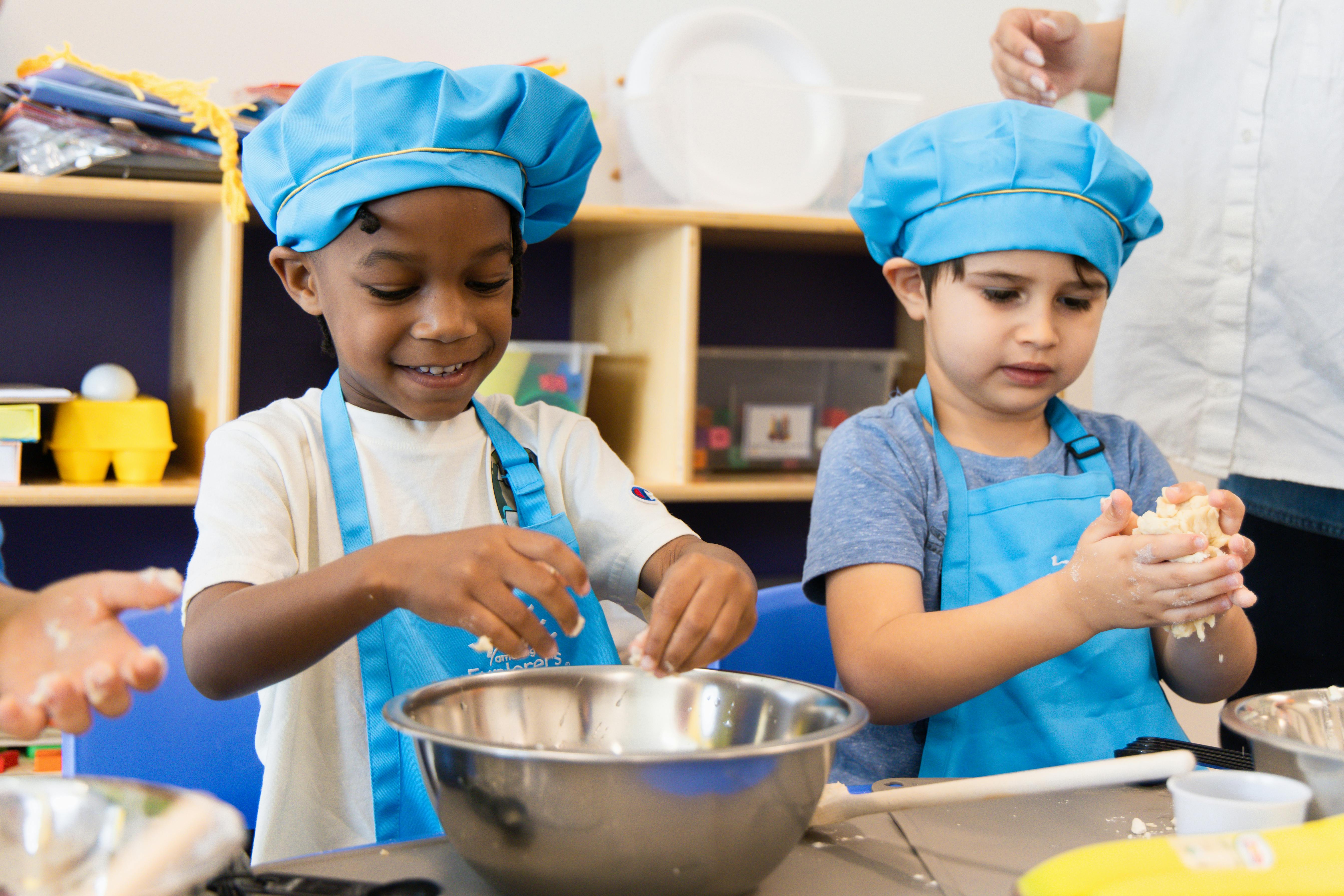 Two children in chef hats and aprons mixing ingredients in bowls