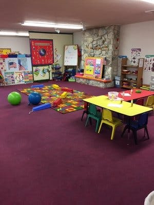 Playroom with colorful rug, toys, and small tables with chairs