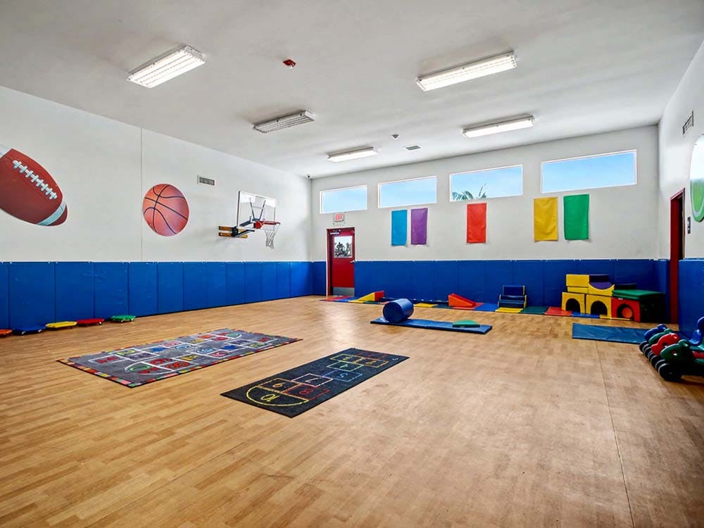 Indoor playroom with mats, colorful equipment, and basketball hoop