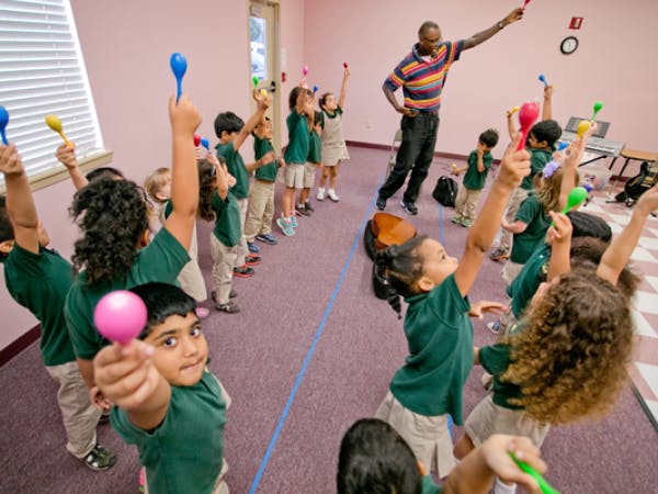 Adult and children holding up colorful maracas in a classroom