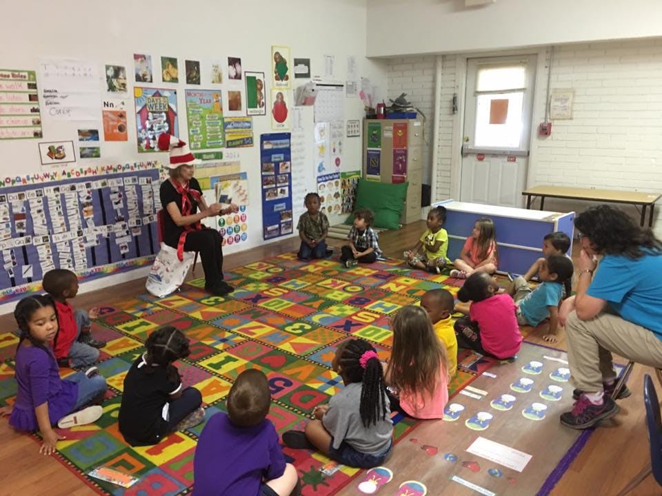 Person in a striped hat reading to children in a classroom