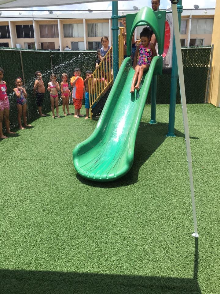 Child going down a green slide with other children standing nearby