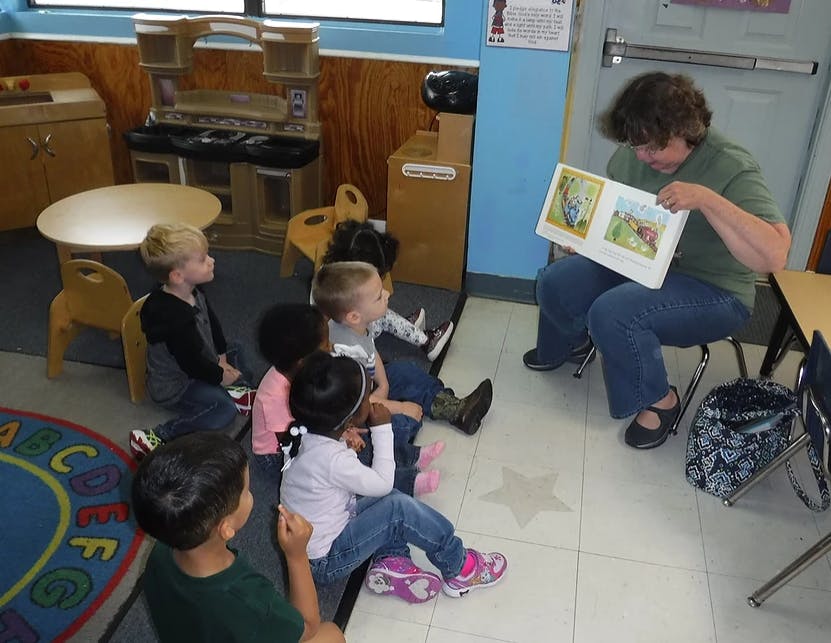 Person reading a book to a group of children in a classroom