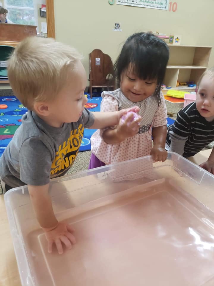 Two children playing with a toy over a clear bin