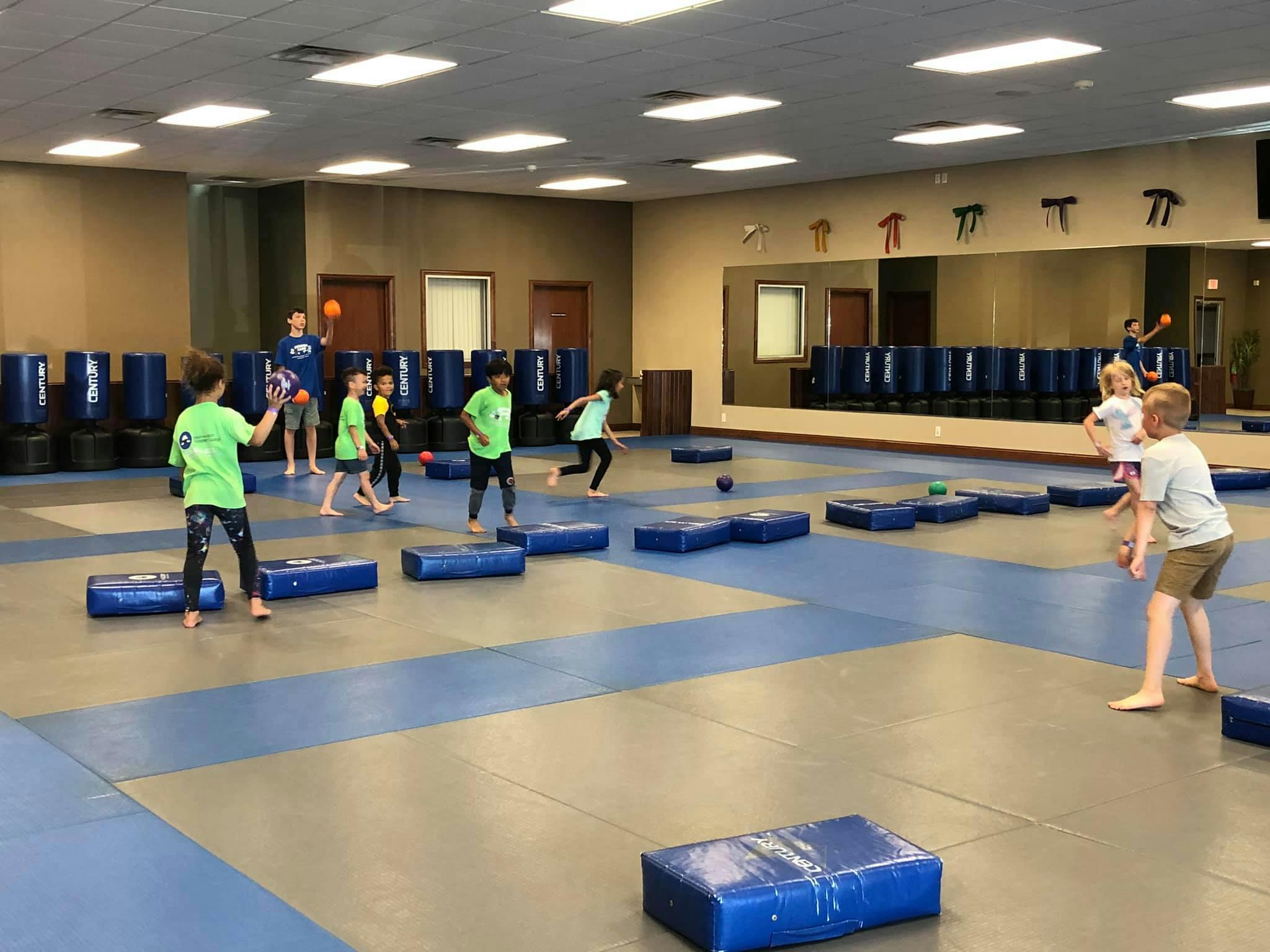 Children playing with balls and blue mats in a large room