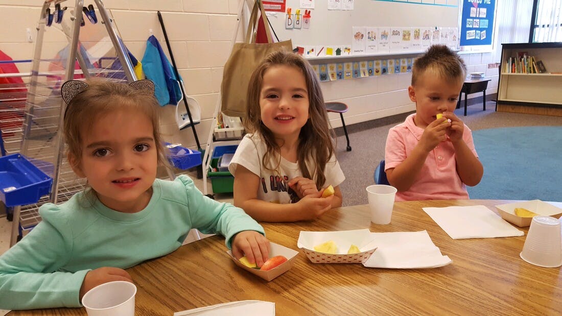 Three children sitting at a table eating snacks