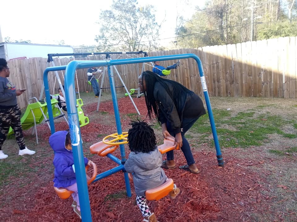 Adults and children on a playground with swings and a seesaw