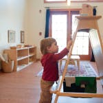 Child reaching up to a wooden easel