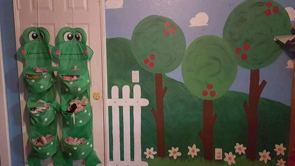 Two green frog-shaped hanging organizers on a door next to a painted mural