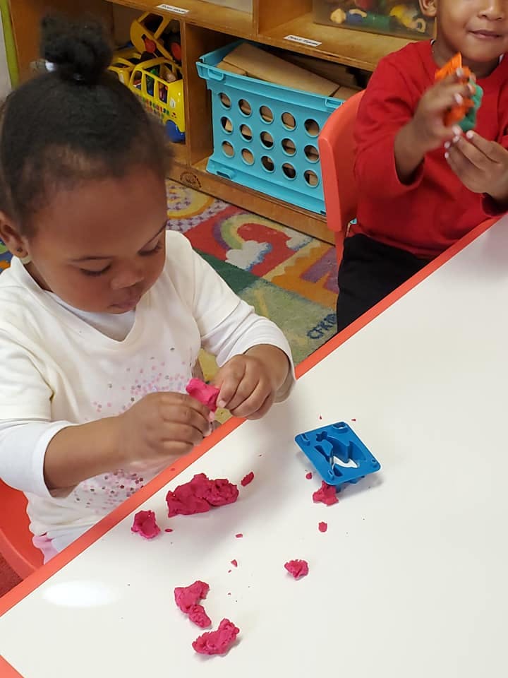 Child playing with red playdough at a table