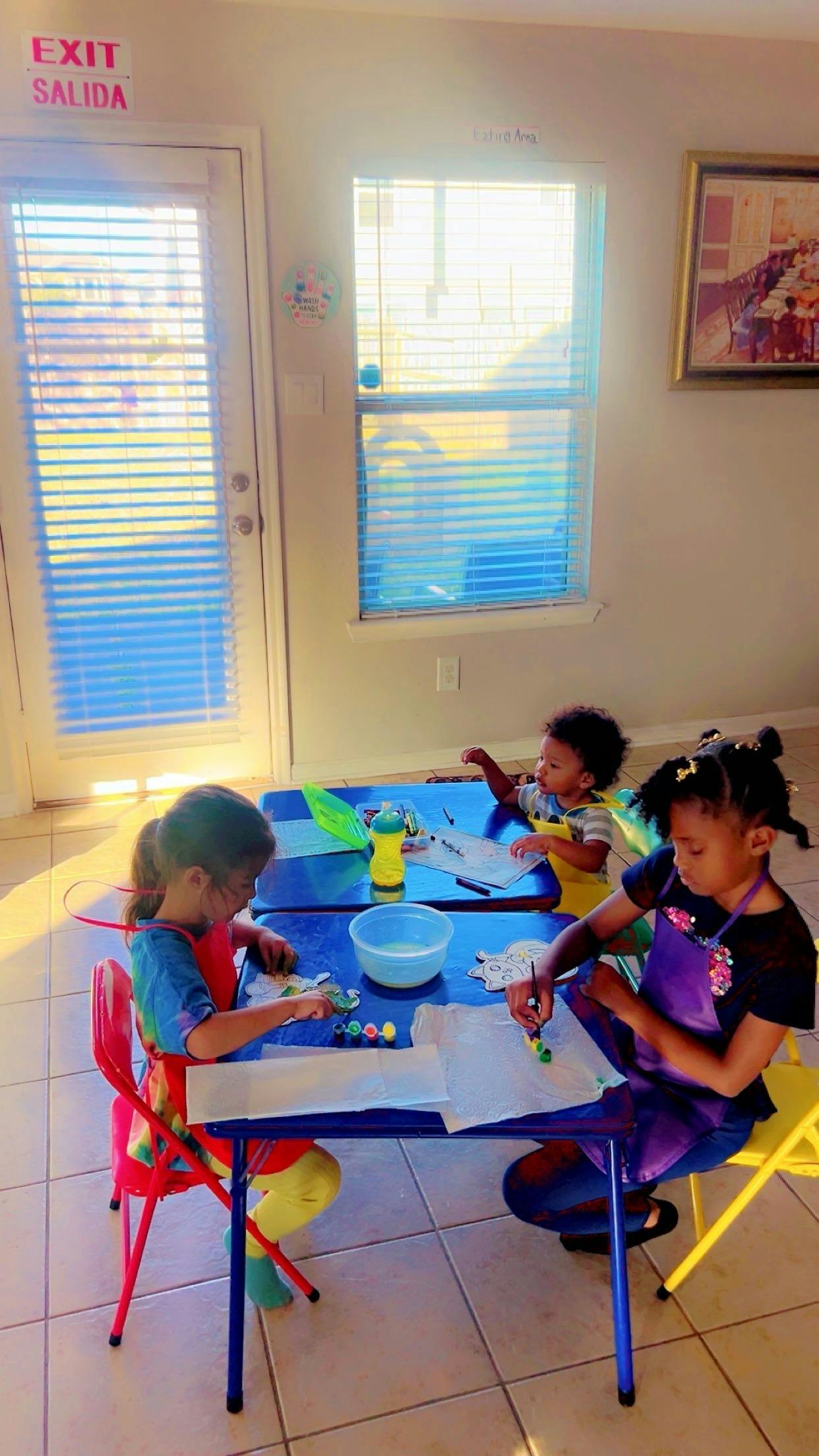 Three children sitting at small tables painting on paper