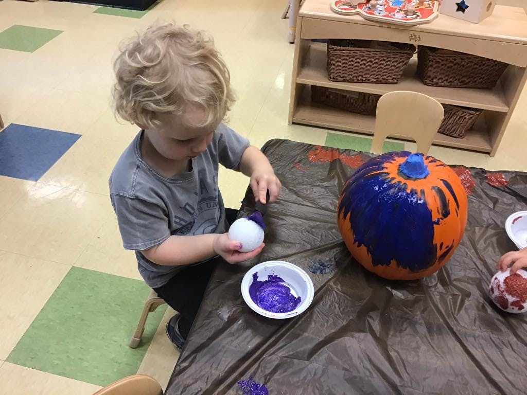 Child painting a small white object with purple paint