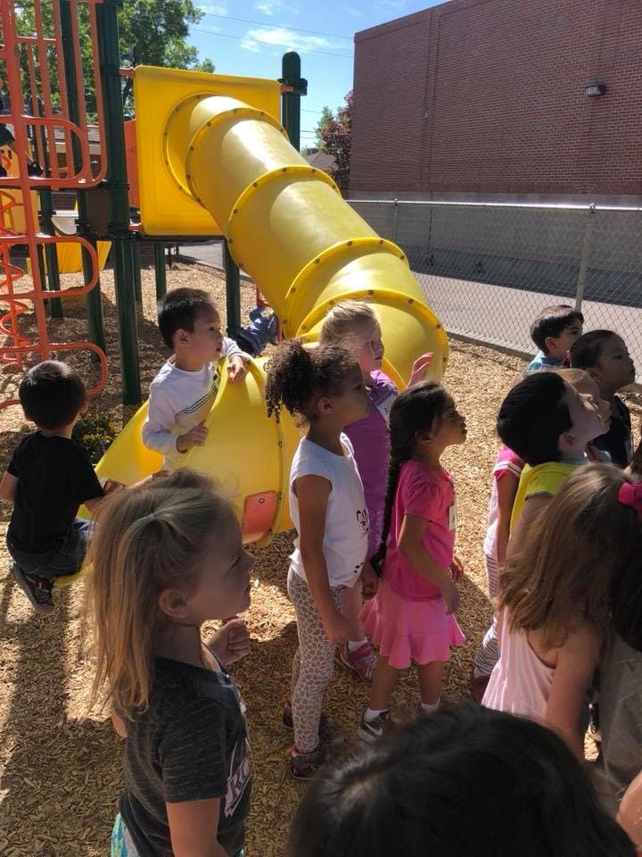 Children standing on a playground near a yellow slide