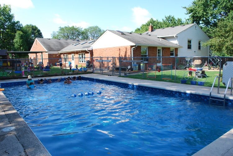 People in a swimming pool next to a fenced yard with houses in the background