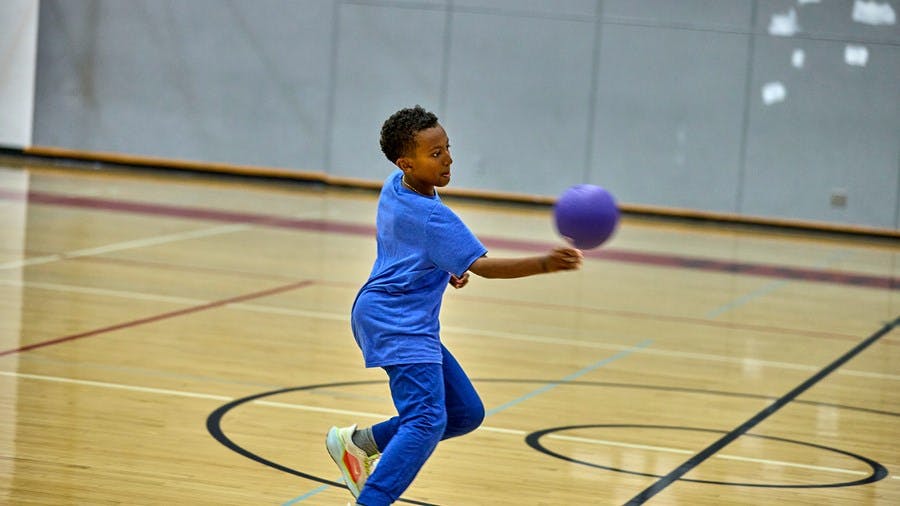 Child throwing a purple ball on a basketball court
