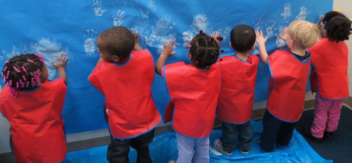 Children in red smocks making handprints on a blue surface
