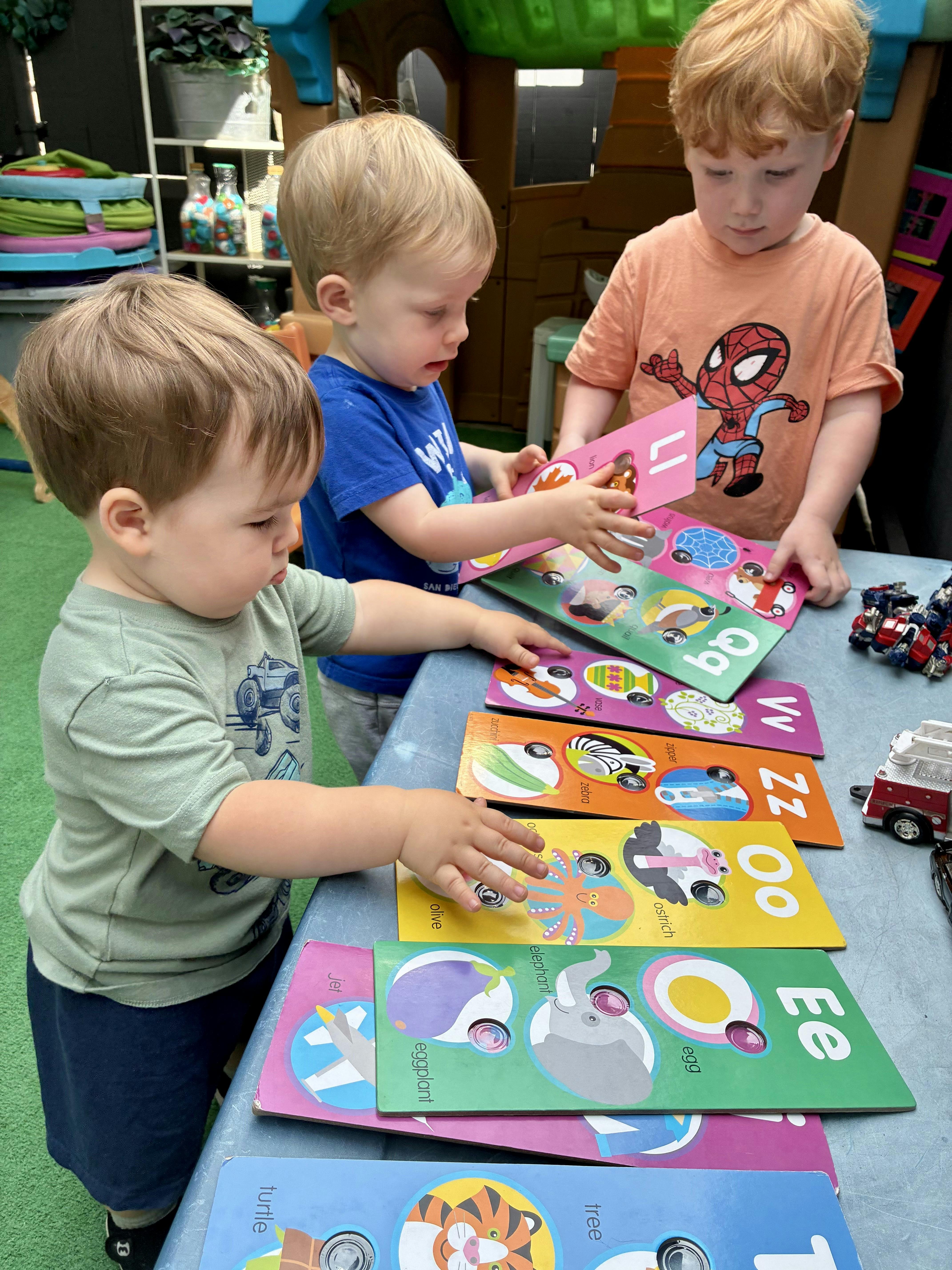 Three children playing with alphabet books on a table