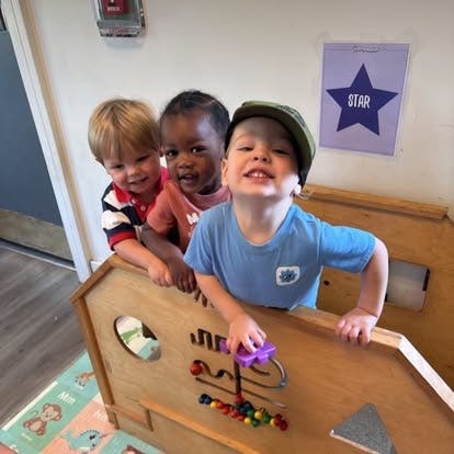 Three children playing with a wooden bead maze in a classroom