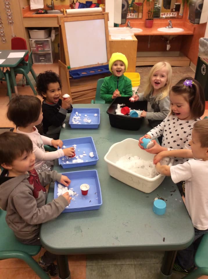 Children playing with artificial snow at a table in a classroom