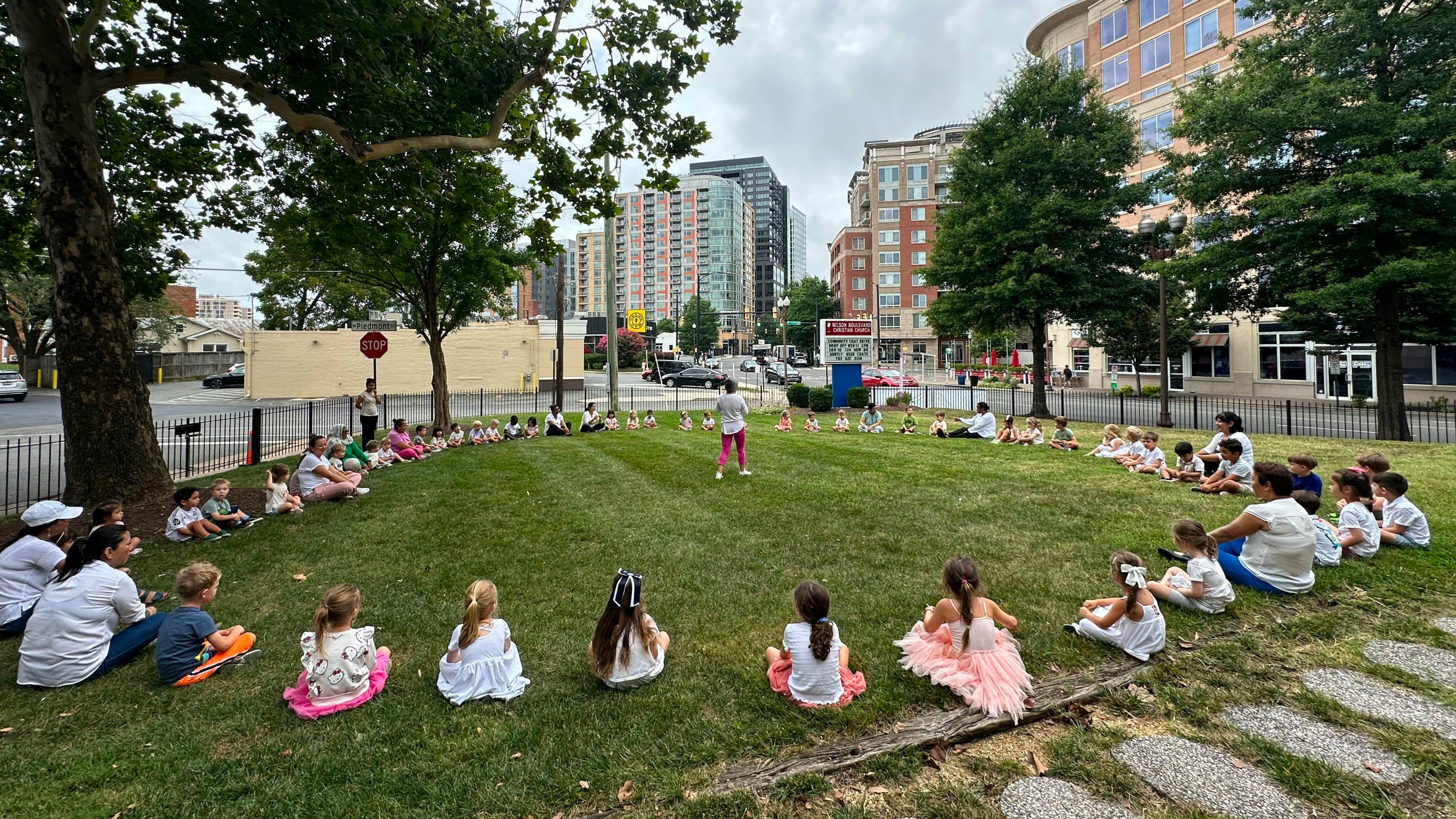Group of children and adults sitting in a large circle on grass outdoors