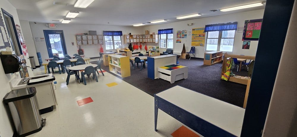 Classroom with small tables and chairs, shelves, and a play area