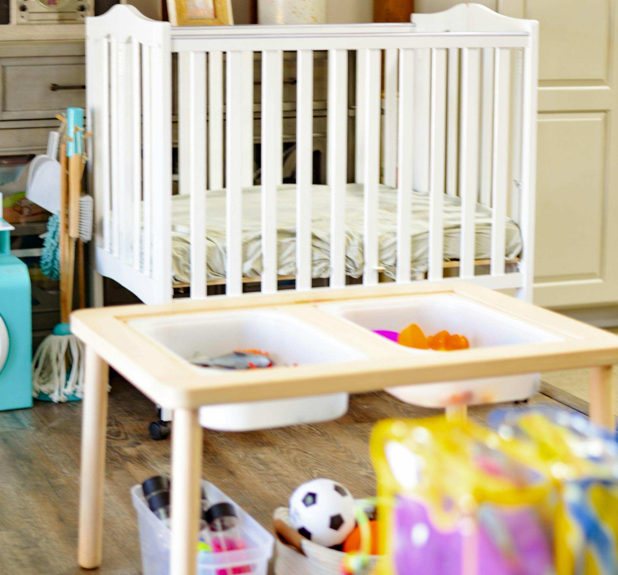 White crib and a wooden play table with toys
