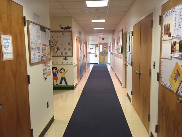 Long hallway with a dark blue runner rug and bulletin boards on the walls