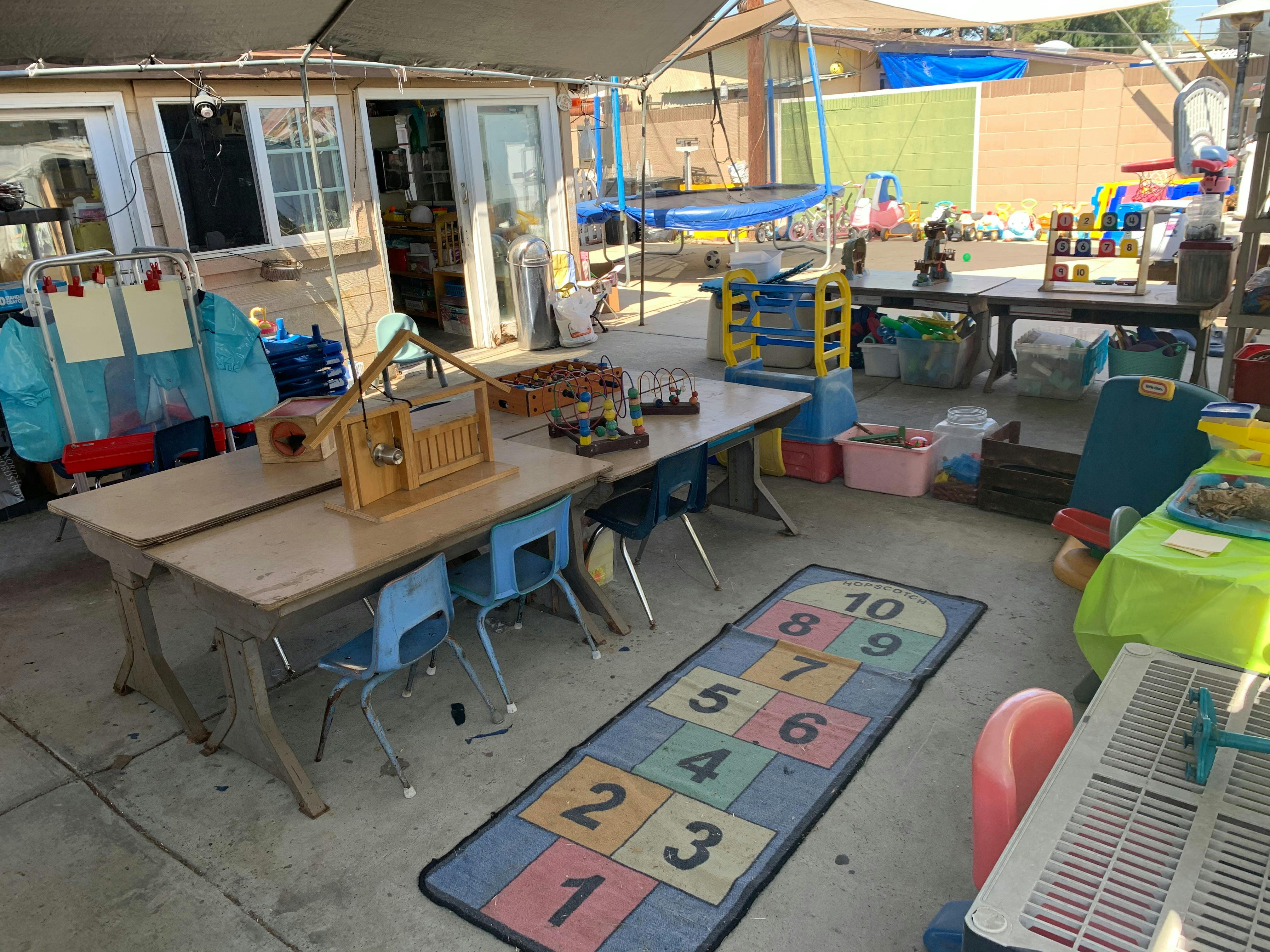 Outdoor play area with tables, chairs, and a hopscotch mat