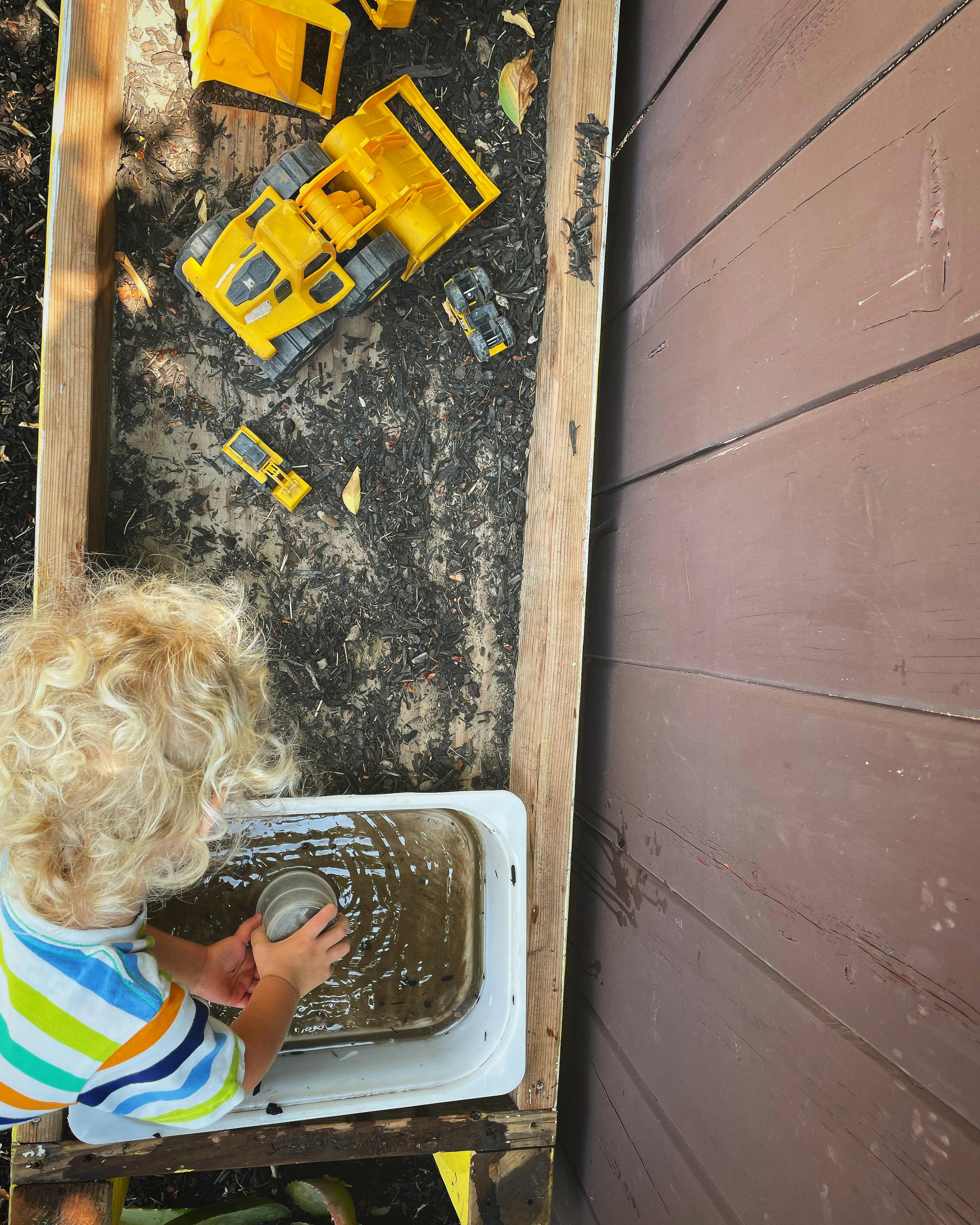 Child playing with water and toy trucks in a wooden trough