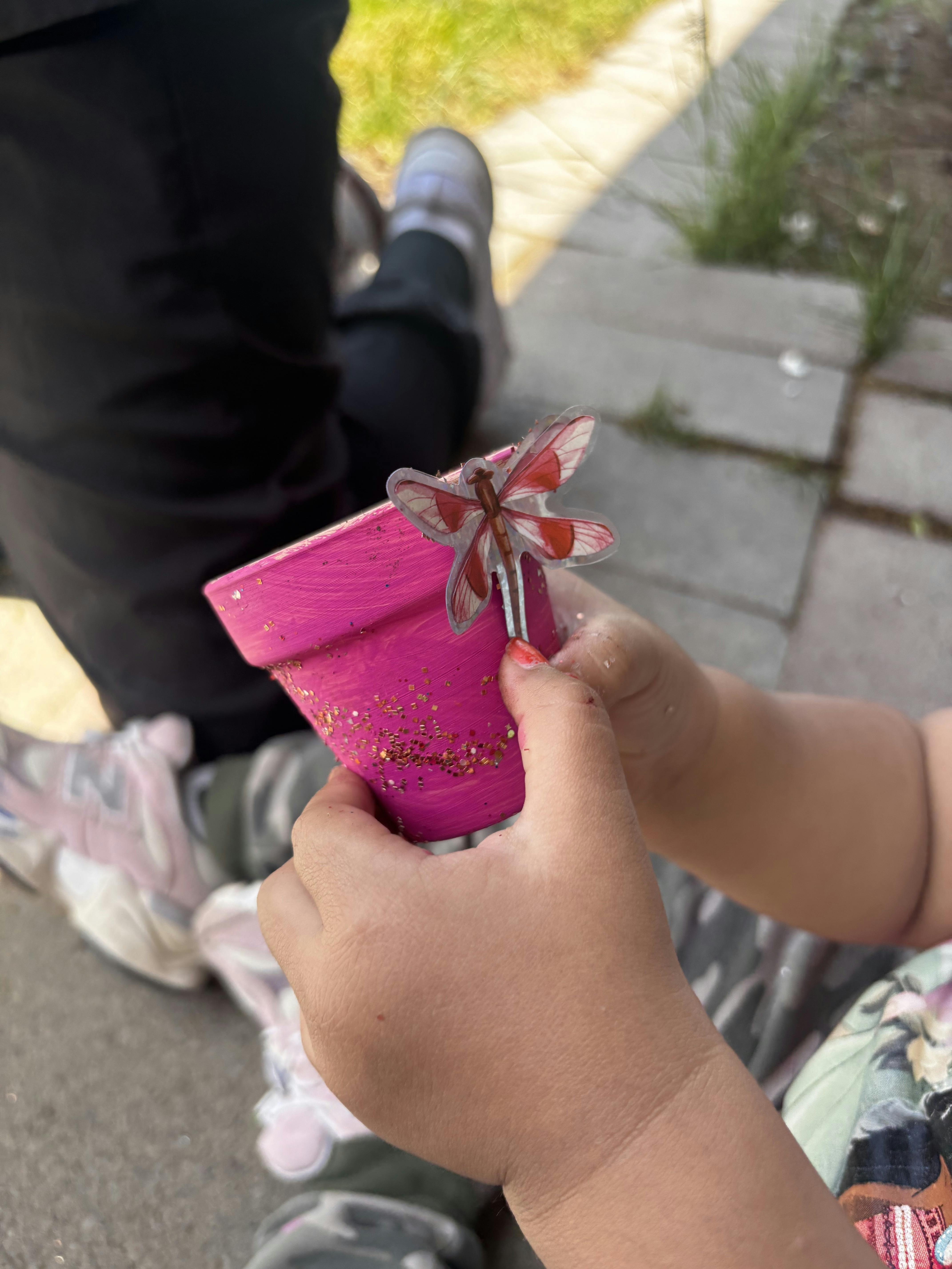 Child holding a small pink flower pot decorated with a dragonfly cutout