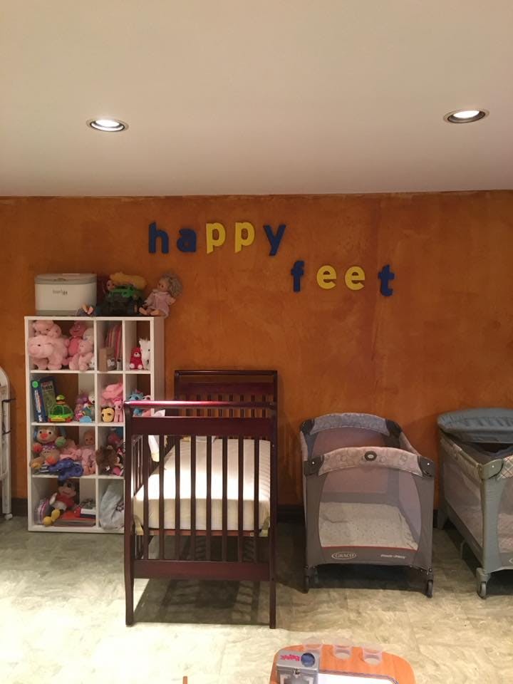 Cribs and playards in a room with "happy feet" on the wall