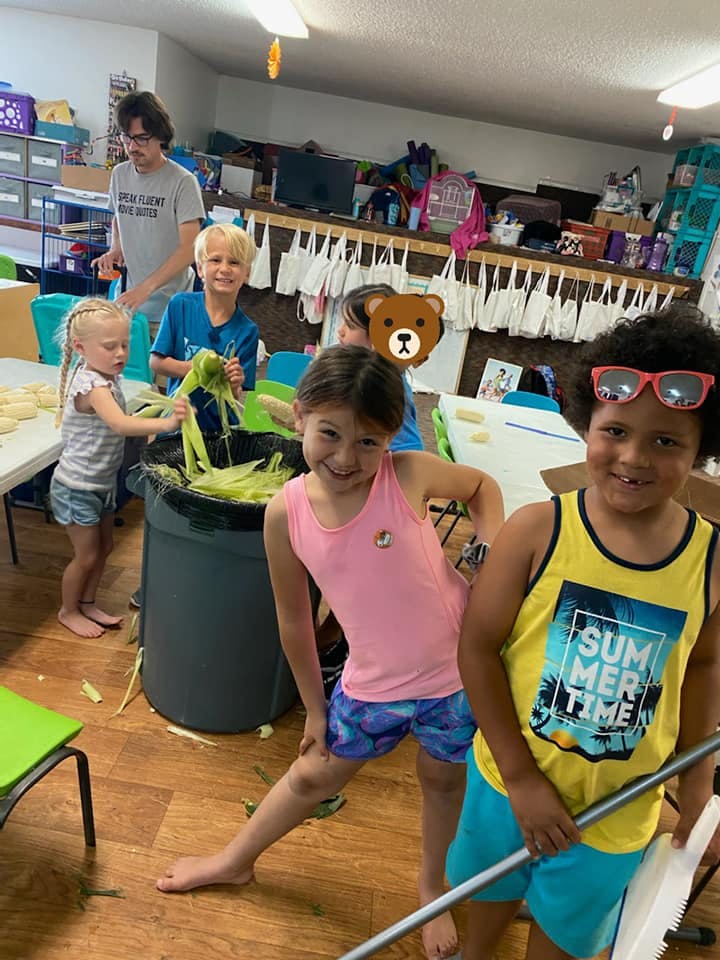 Children shucking corn into a large bin