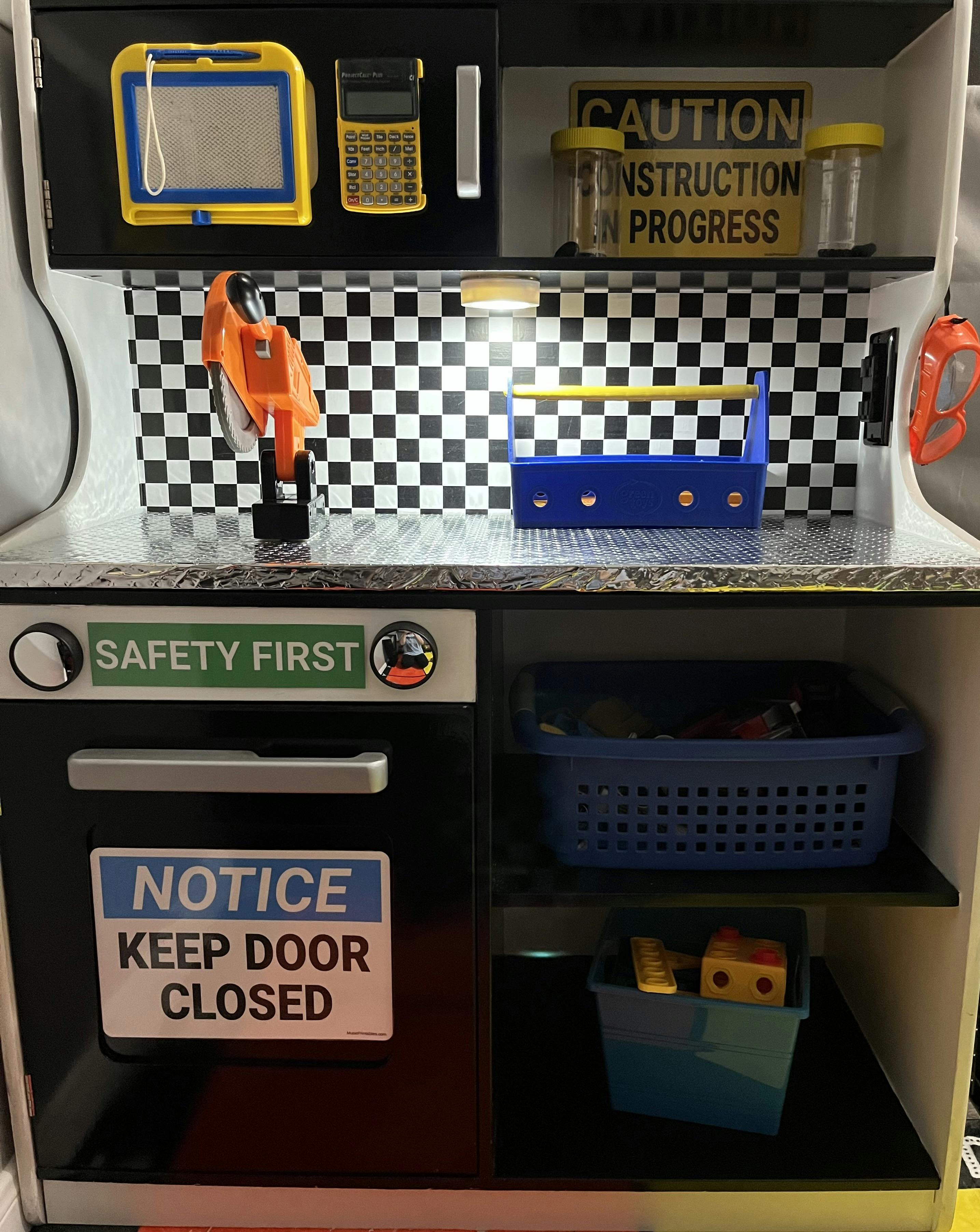 Toy workbench with tools and signs that say "Safety First" and "Notice Keep Door Closed"