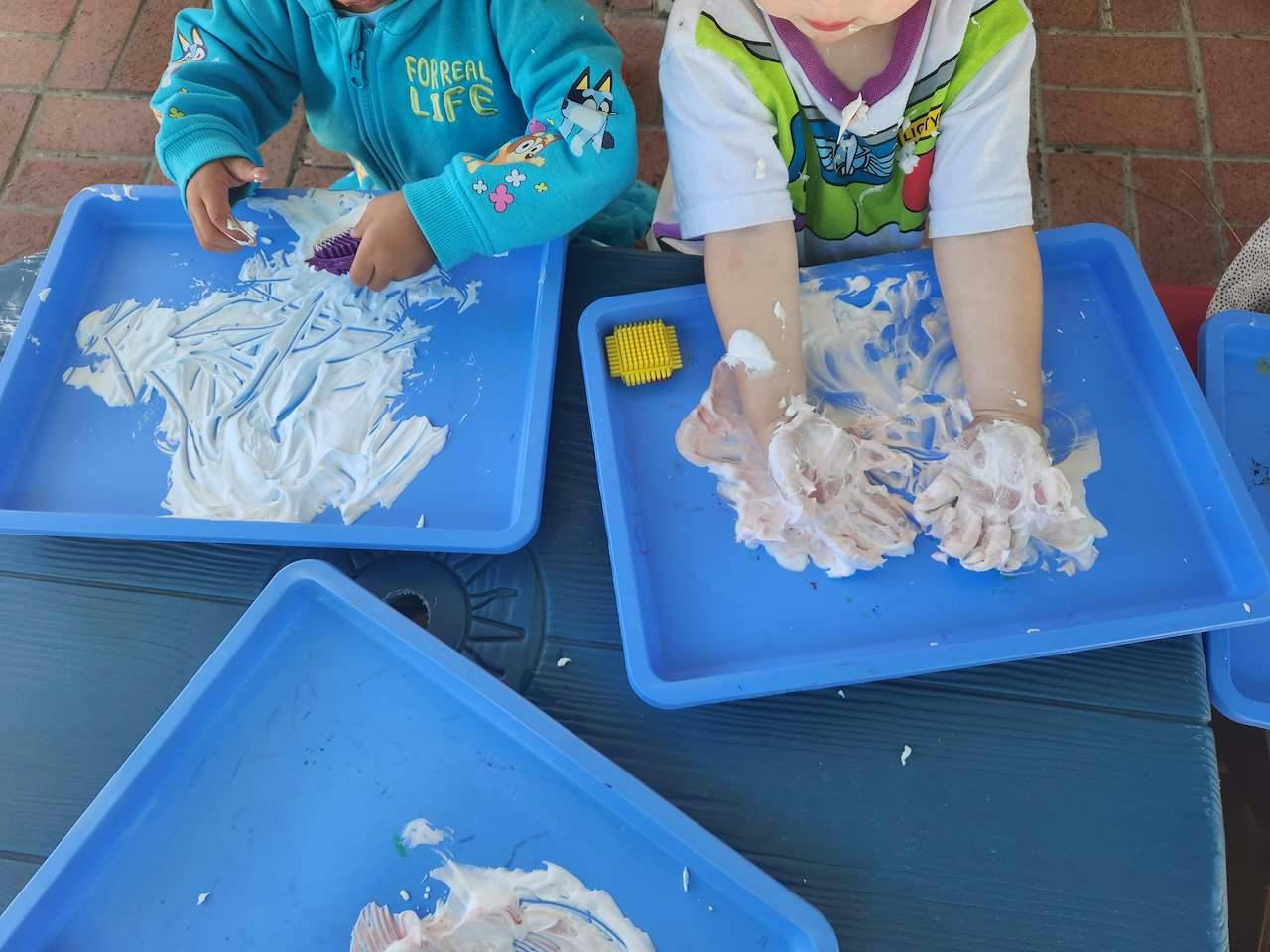 Children playing with shaving cream on blue trays
